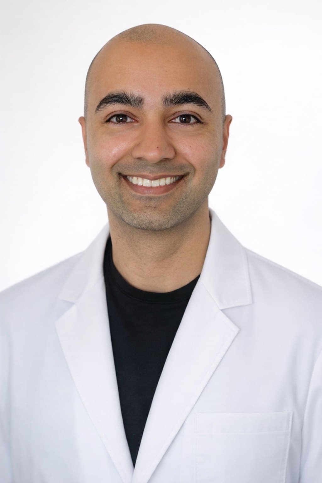 Karim Ali in a white coat against a plain light background.